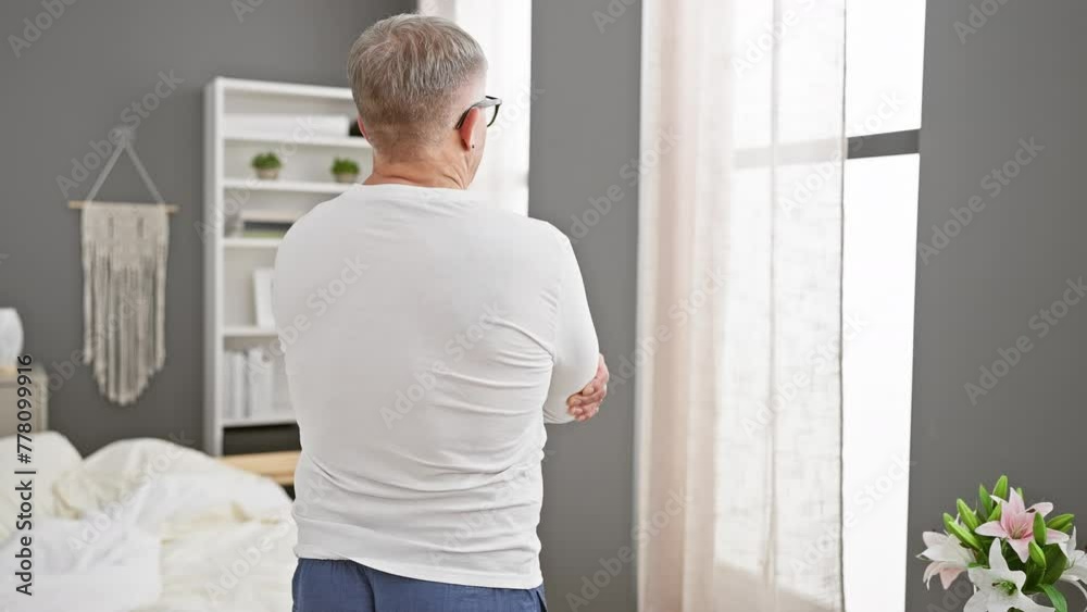 Canvas Prints Mature grey-haired man lost in thought, standing backwards with crossed arms in bedroom, clad in pyjamas