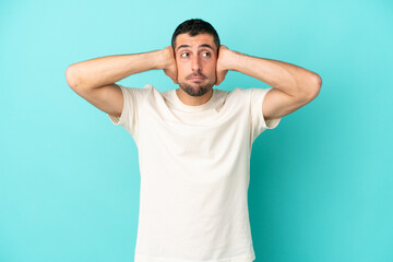 Young handsome caucasian man isolated on blue background frustrated and covering ears