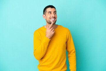 Young handsome caucasian man isolated on blue background looking up while smiling