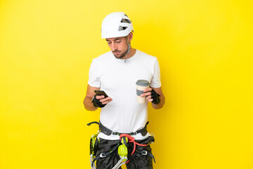 Young rock- climber man isolated on yellow background holding coffee to take away and a mobile