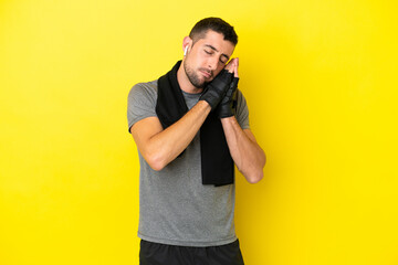 Young sport caucasian man isolated on yellow background making sleep gesture in dorable expression