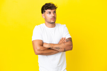 Young caucasian handsome man isolated on yellow background making doubts gesture while lifting the...