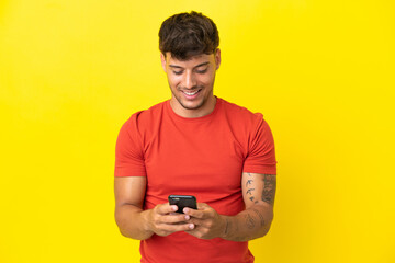 Young caucasian handsome man isolated on yellow background sending a message with the mobile