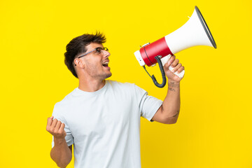 Young caucasian handsome man isolated on yellow background shouting through a megaphone to announce...
