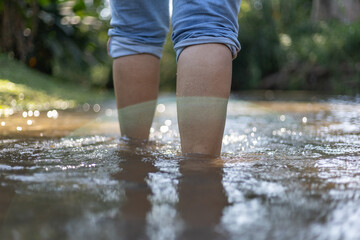 Selective focus of woman's legs folded, pants legs walking, wading in water in a natural forest