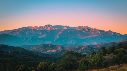 The last rays of the sun cast a pink alpenglow on the mountain range, highlighting the layered landscape.