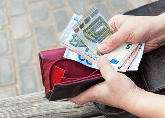 Pink purse, banknotes and coins in female hands, selective focus.	