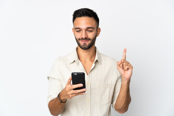 Young caucasian man isolated on white background using mobile phone and lifting finger