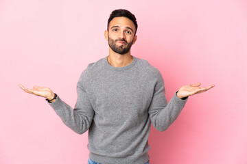 Young caucasian man isolated on pink background having doubts while raising hands - obrazy, fototapety, plakaty