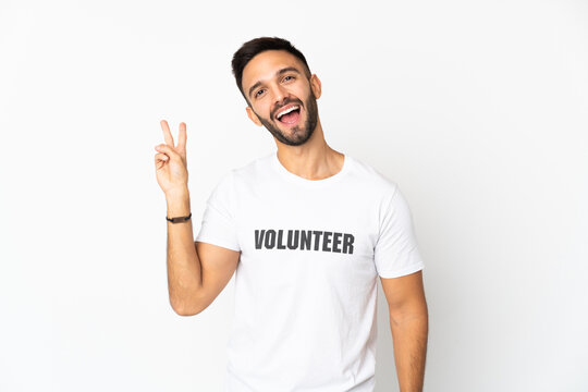Young caucasian volunteer man isolated on white background smiling and showing victory sign