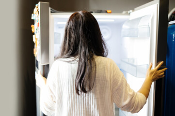 Sad woman looking into her empty fridge with no groceries