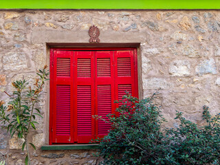 A classic design house window with bright red shutters on rough stone walls and a green stripe at the top. Travel to Athens, Greece. - 778115168