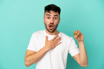 Young man holding a Bitcoin isolated on blue background surprised and shocked while looking right