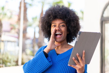 African American girl holding a tablet at outdoors shouting with mouth wide open