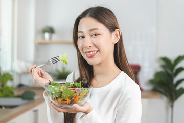 Diet, Dieting concept asian young woman hand use fork at green oak on mix vegetables, salad bowl in the kitchen, eat  food is low fat good health. Nutritionist female, Weight loss for healthy person. - obrazy, fototapety, plakaty