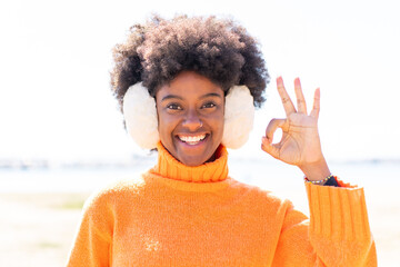 African American girl wearing winter muffs at outdoors showing ok sign with fingers