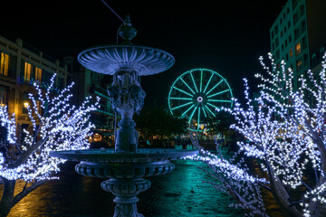 Grande roue illuminée en vert devant une fontaine la nuit à Noël