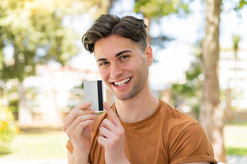 Young handsome man holding a credit card and pointing it