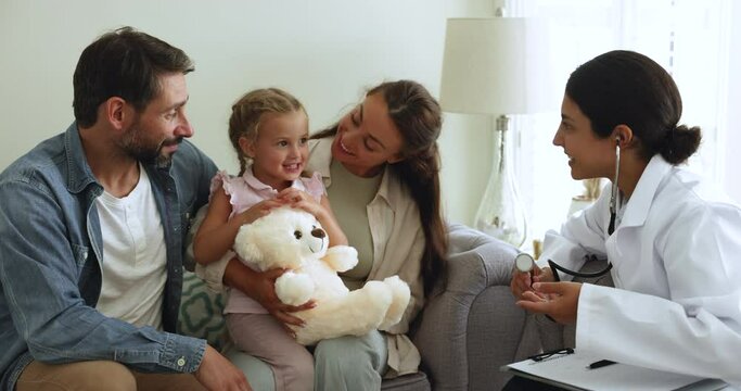 Loving spouses brought their little daughter to doctor for regular health check up examination. Smiling female Indian pediatrician talk to parents of small kid at home-call visit. Medicine, pediatry