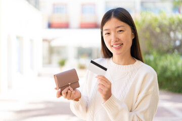 Fototapeta na wymiar Pretty Chinese woman at outdoors holding wallet and credit card with happy expression