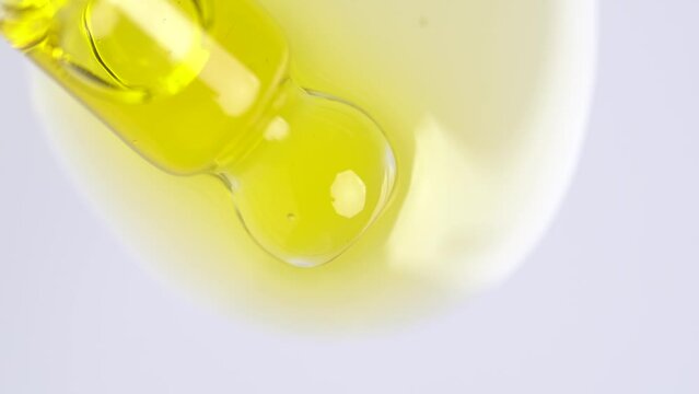 Liquid fluid yellow oil, gel or serum on a white surface. Pipette with orange cosmetic fluid with bubbles, macro shot.
