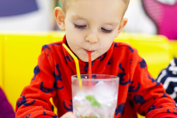 Little boy sipping water with mint leaves through a straw from a clear glass