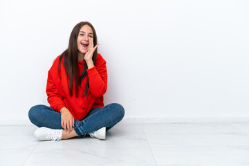 Young Ukrainian woman sitting on the floor isolated on white background shouting with mouth wide...