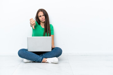 Young Ukrainian woman with a laptop sitting on floor showing thumb down with negative expression