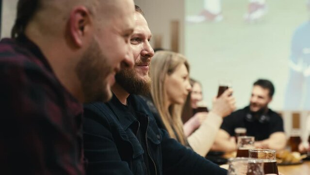 A group of friends in a sports bar are drinking beer and eating beer snacks while cheering on a football team playing in a tournament. Supporting fans cheer, cheer and shout in a sports pub.