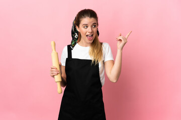Young blonde woman holding a rolling pin isolated on pink background intending to realizes the...
