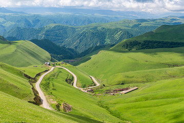 landscape with green hills,  blue sky andmountain road in sunny valley