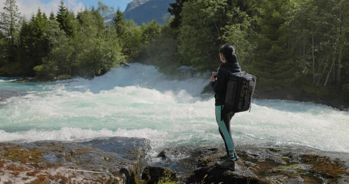 Female traveler with a backpack, drinking water in nature in the forest near a mountain river.