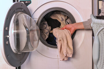 Man putting clothes in the washing machine with the laundry basket next to it, unrecognizable,...
