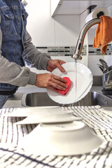 Man washing dishes with sponge in the kitchen, with some stacked next to him, unrecognizable, side view, vertical. Concept of male doing housework