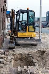 mini excavator stands outside on the street with a hole in the foreground