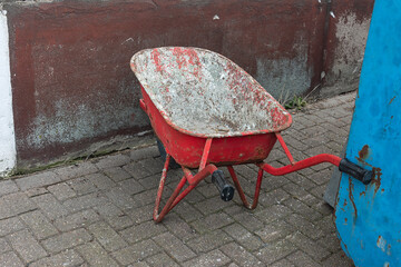 weathered red industrial wheelbarrow stands outside on paving stones