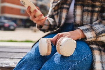 One young girl is listening to music on her wireless headphones and using her phone outdoors on a sunny day	
