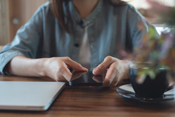 Close up of, woman sitting at wooden table using mobile phone in coffee shop, front view. Woman using smartphone for mobile banking, online shopping, social media network