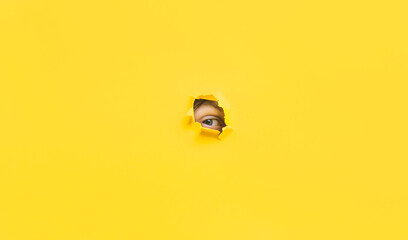 A right eye looking through a hole in a yellow paper. Voyeurism. The man is watching the wife. A curious look. Jealousy, spying on or overhearing the concept. Copy space. - obrazy, fototapety, plakaty