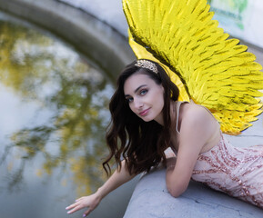 Artistic photo A fantasy female angel with golden wings looks at the background of architecture. Fairy girl sexy lady fashion model pose