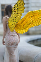 Artistic photo A fantasy female angel with golden wings looks at the background of architecture. Fairy girl sexy lady fashion model pose