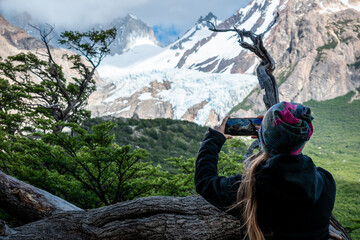 Mujer senderista tomando fotogafia con su celular a lejano glaciar, en su recorrido por los...