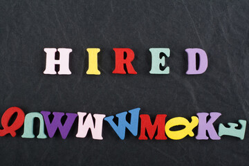 HIRED word on black board background composed from colorful abc alphabet block wooden letters, copy...