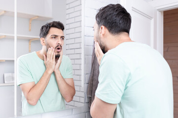 Young funny man looking at the mirror after morning routine in the bathroom	