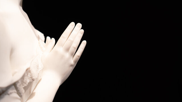 Close-up on female hands in prayer of marble statue