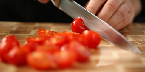 Cook holds knife in hand and cuts on cutting board red tomatoes for salad or fresh vegetable soup...