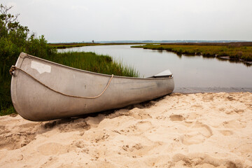 A canoe is sitting on the beach next to a body of water