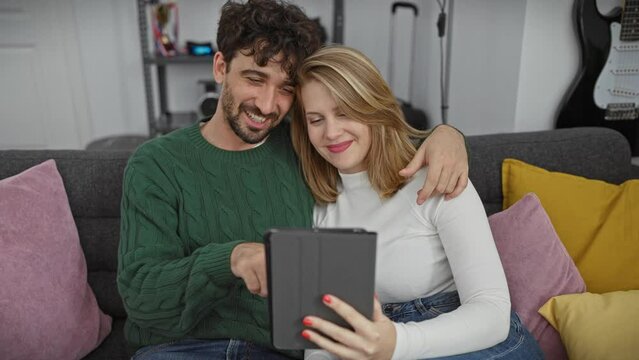 A loving couple enjoys using a tablet together on a cozy, colorful living room sofa.