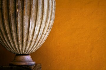 Side detail of a heavy marble vase, with an orange textured background. 