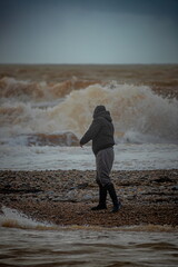 Man on the pebble beach of Jurassic Coast near town of Seaton, Eat Devon watching big wave during...